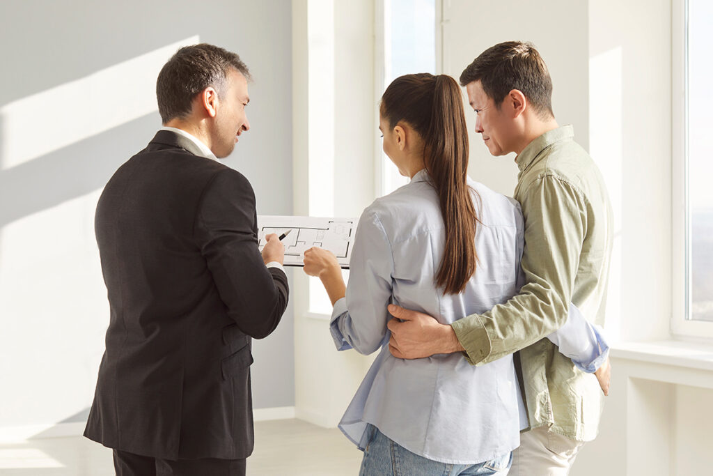 Real estate agent presenting an apartment layout to a smiling young couple, symbolizing personalized support after purchase