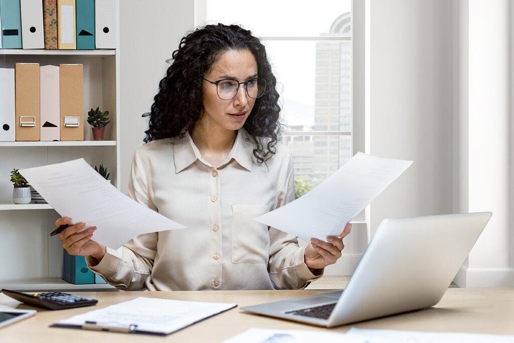 Businesswoman intently reviewing documents at desk in modern office setting with serious expression