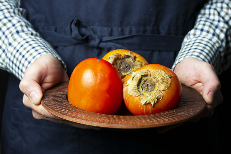 Farmer holds fresh persimmon, a seasonal fruit for autumn.