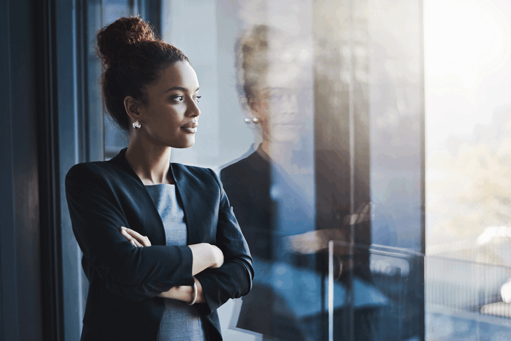 Female business woman looking out of an office window into the distance.