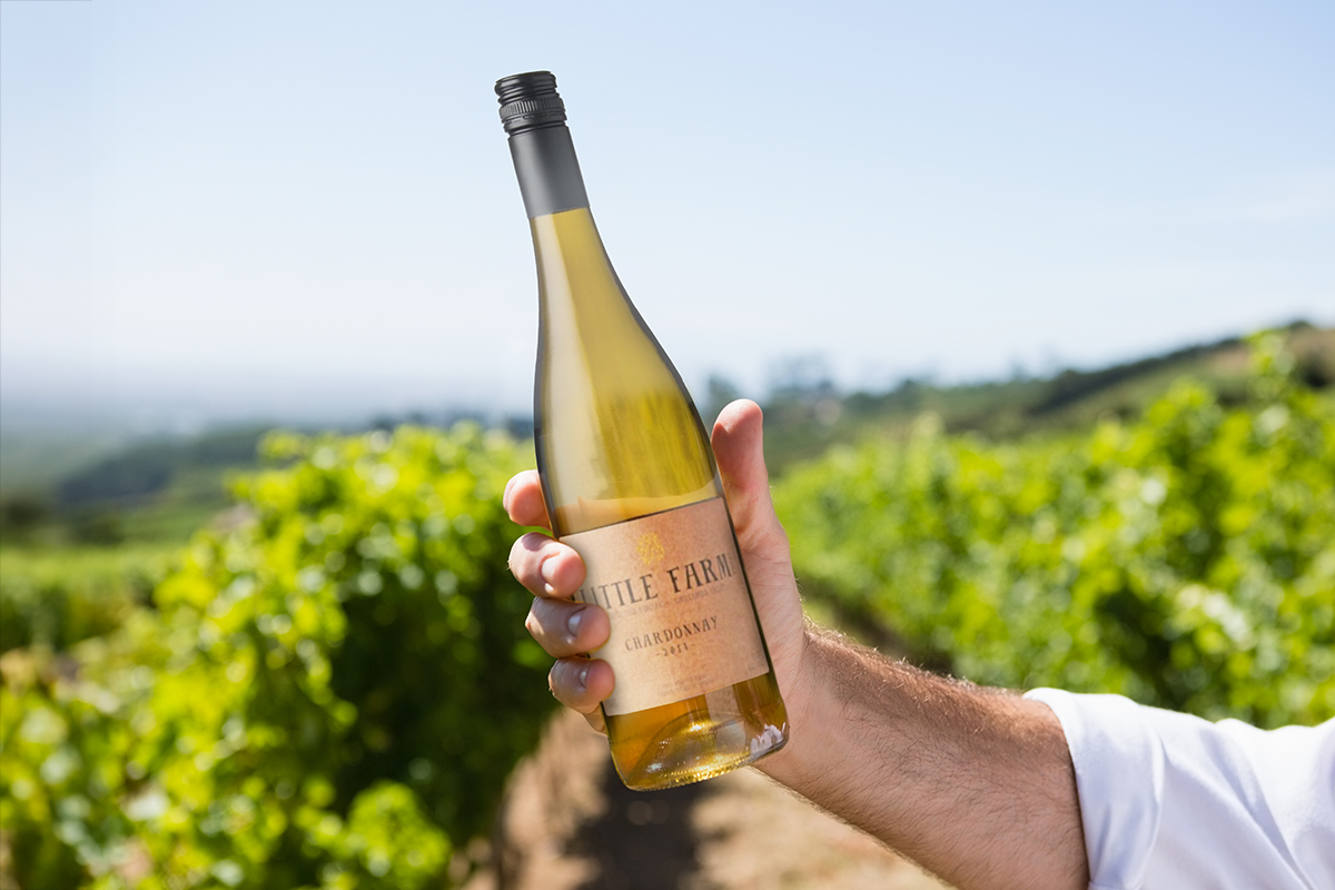 Bottle of Little Farm Chardonnay held in the fields of a Canadian winery