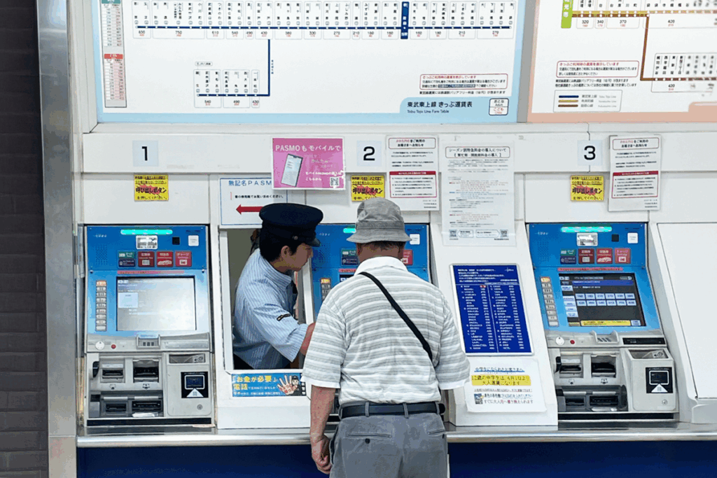 Train station booth attendant pops his head out next to the ticket machine to assist a passenger
