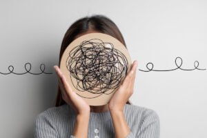 Woman holding a drawing of tangled lines in front of her face, symbolizing mental stress and finding calm through acceptance and self-awareness.
