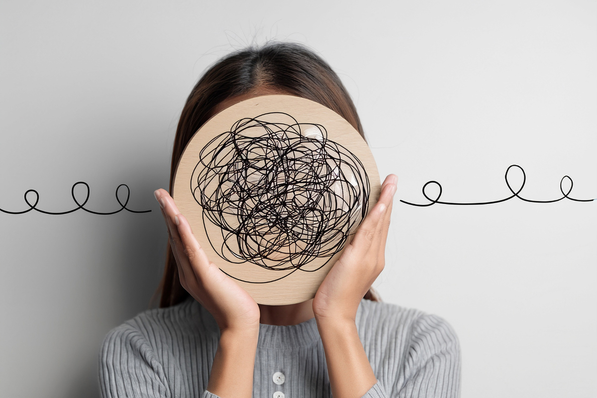 Woman holding a drawing of tangled lines in front of her face, symbolizing mental stress and finding calm through acceptance and self-awareness.