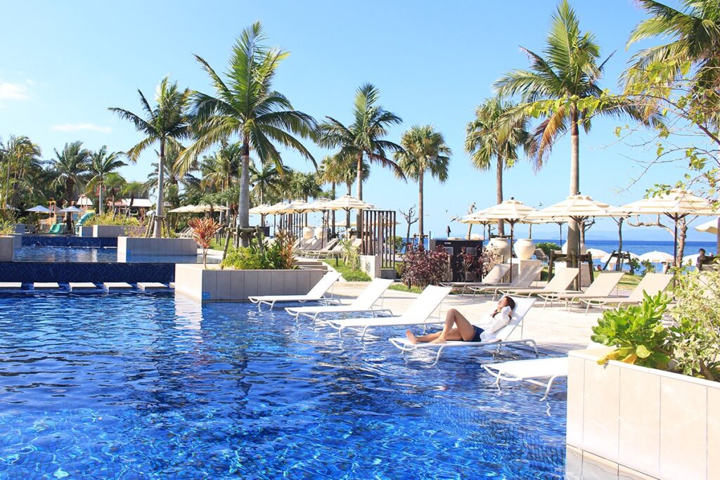 woman relaxing at a luxurious a pool with deck chair and palm trees in Okinawa's Fusaki Beach Resort