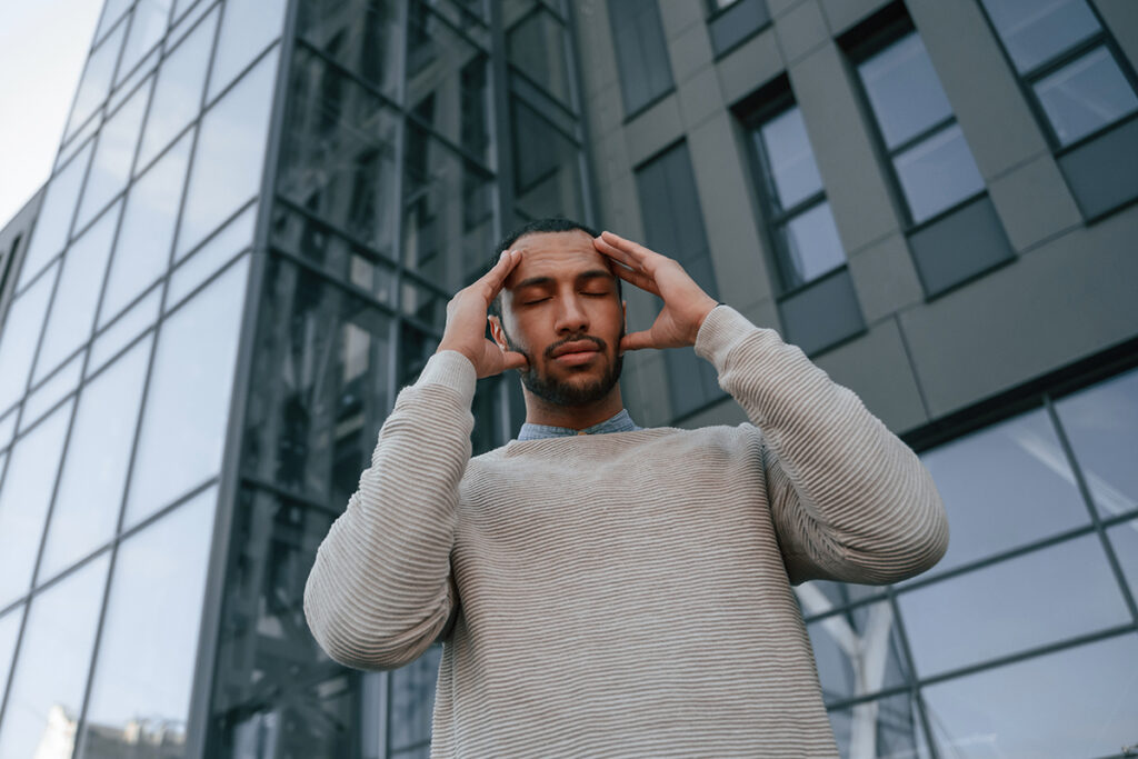 Man is outdoors surrounded by office buildings, feeling bad and showing signs of stress. 